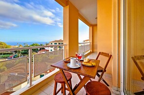 Ein Balkon mit Tisch für zwei Personen, einem Stuhl und Blick auf das Meer und die Gebäude.