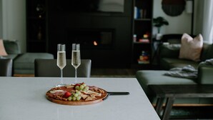 Una mesa de comedor con una tabla de embutidos, dos copas de champán y una chimenea al fondo.