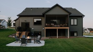 Una casa moderna de dos pisos con un porche cubierto, un brasero y mobiliario exterior.