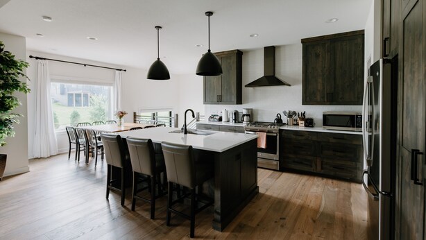 Una cocina moderna con una isla central, armarios de madera oscura, electrodomésticos de acero inoxidable e iluminación colgante.