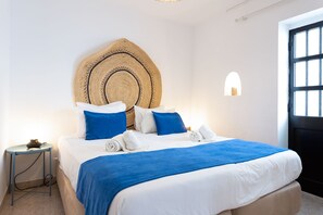 A neatly made bed with a blue and white bedspread, a woven headboard, and a bedside table with a lamp.