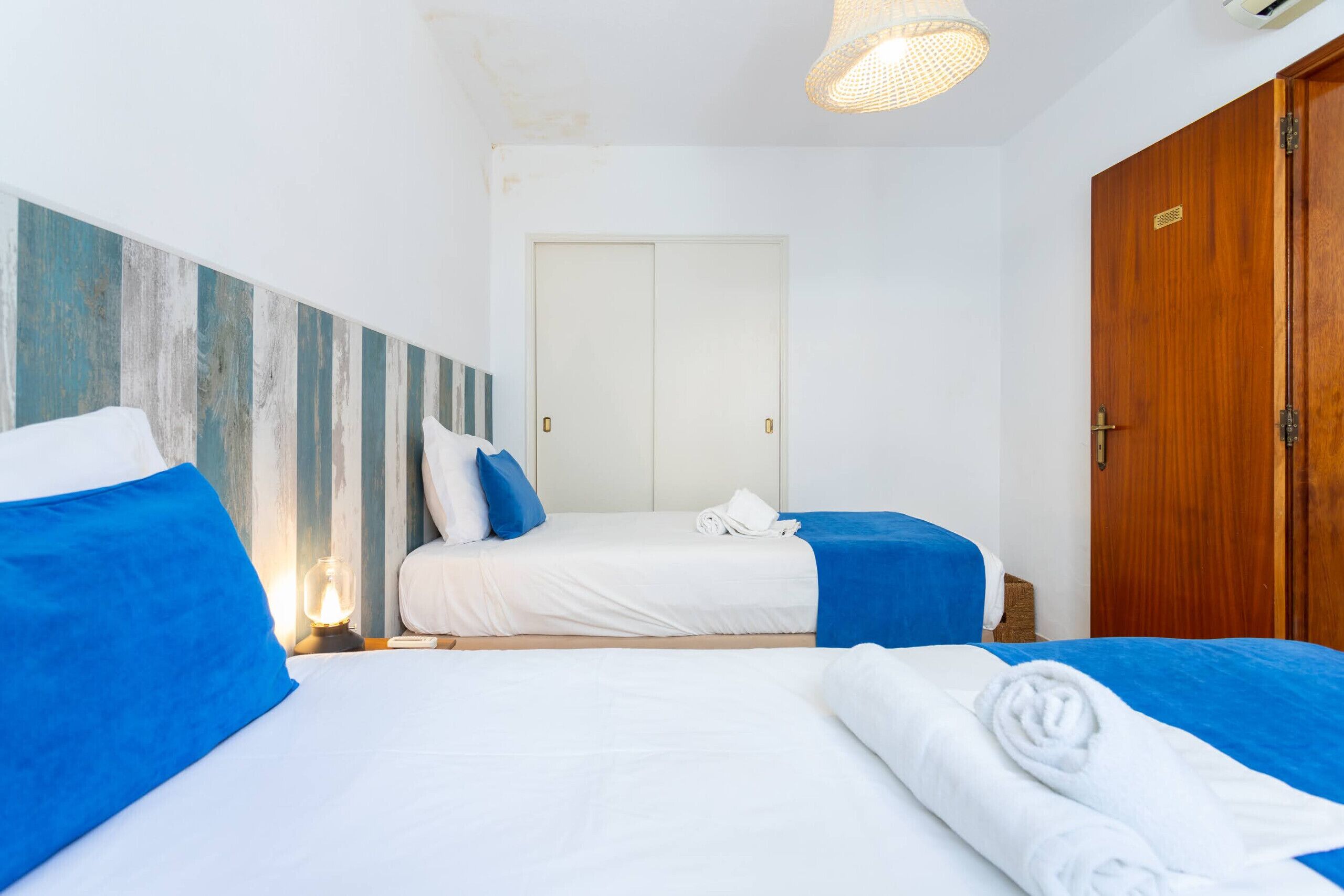 A hotel room with two beds, a wooden door, and a white wall with a blue and white striped pattern.