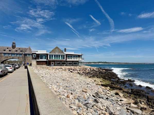 A coastal building with a stone archway, a modern extension with large windows, and a rocky shoreline.