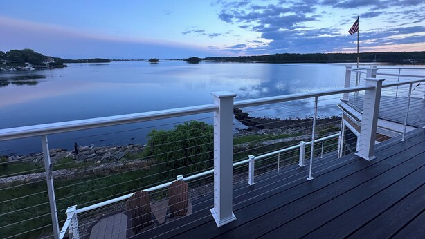 A deck with a railing overlooking a calm lake with distant islands and a clear sky.
