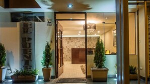 L’entrée d’un hôtel, avec un comptoir d’accueil, un panneau indiquant « VISA » et des plantes en pot.