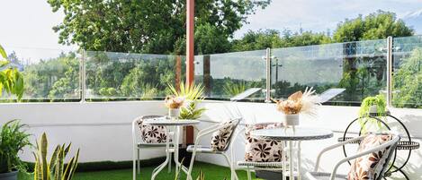 Un patio techado con mesa y sillas, plantas en macetas y vistas del entorno verde.
