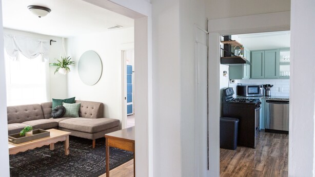 A modern living room with a sofa, coffee table, and a small rug. A kitchen with wooden flooring and stainless steel appliances is visible through an open doorway. - Double Everything - Sleeps 13

 (Fort Worth)