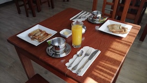 A breakfast table with toast, a glass of orange juice, a small bowl of butter, and a metal cup. - Hotel Cesare (Uyuni)