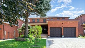 A two-story brick building with a garage, a paved driveway, and a small lawn with a tree. - Stunning 2BR Lower Level Unit

 (Richmond Hill)