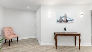 A room with a wooden floor, a pink upholstered chair, a wooden table with a potted plant, and a wall-mounted picture of a bridge. - Stunning 2BR Lower Level Unit

 (Richmond Hill)