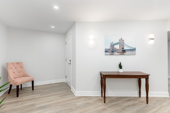 A room with a wooden floor, a pink upholstered chair, a wooden table with a potted plant, and a wall-mounted picture of a bridge. - Stunning 2BR Lower Level Unit
(Richmond Hill)