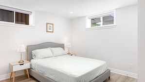 A bedroom with a bed, two bedside tables, a nightstand, a window, and a picture on the wall. - Stunning 2BR Lower Level Unit

 (Richmond Hill)