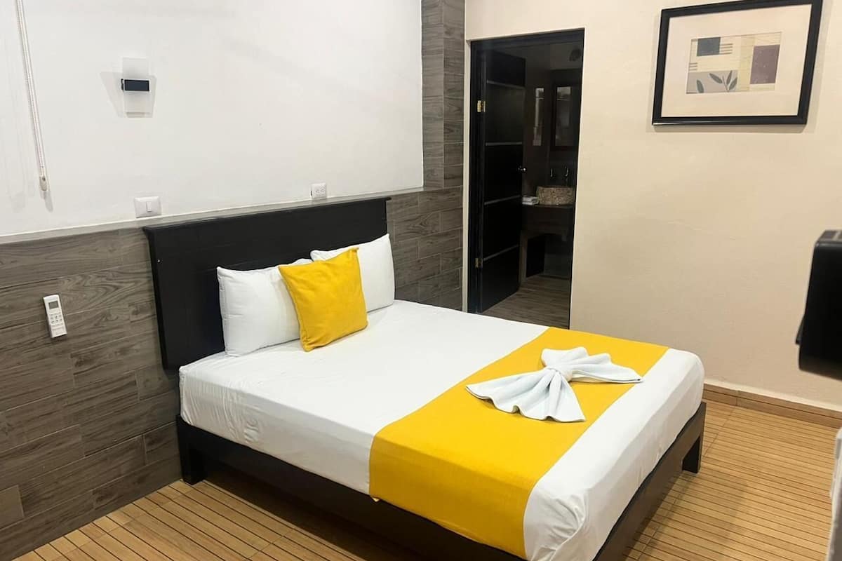 Quarto de hotel com cama, mesa de cabeceira, espelho e um quadro pendurado na parede.