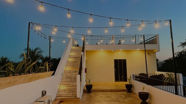 Un edificio moderno con una escalera que lleva a un balcón, luces colgantes y plantas en macetas.