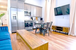 Een compacte keuken met moderne apparatuur, een eethoek met een houten tafel en metalen stoelen, en een flatscreen televisie aan de muur.