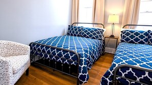Un dormitorio con dos camas, una mesita de noche, una lámpara y una silla.