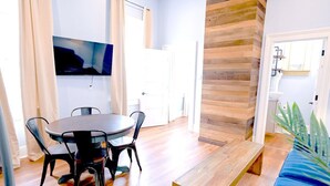 A modern living room with a round dining table, black chairs, a wooden bench, and a flat-screen TV mounted on the wall. - Governors Apartment -  2 bedroom  - Steps to FQ (New Orleans)