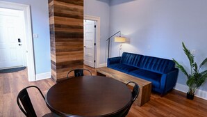 Una habitación con una mesa redonda de madera, dos sillas, un sofá azul y una lámpara de pie.