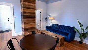 A room with a round wooden table, two chairs, a blue sofa, and a floor lamp.