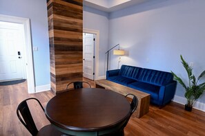 A room with a round wooden table, two chairs, a blue sofa, and a floor lamp.