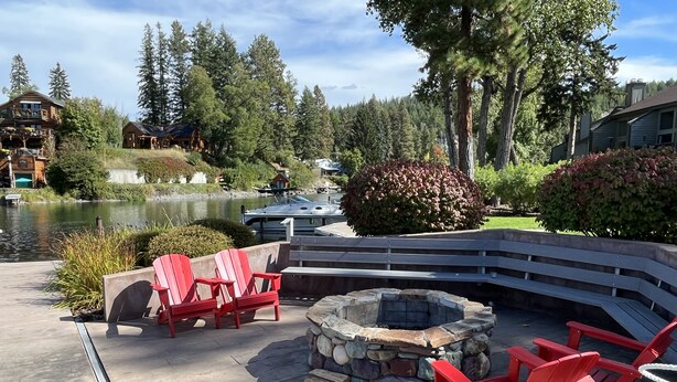 A lakeside patio with red Adirondack chairs, a stone fire pit, and a view of a lake and boats. - Best Value. Large 2 Bedroom Condo in Bigfork, Montana. Perfect Summer Getaway!  (Bigfork)
