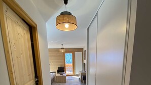 Un corridoio con una porta in legno, pavimento piastrellato e una lampada a sospensione.
