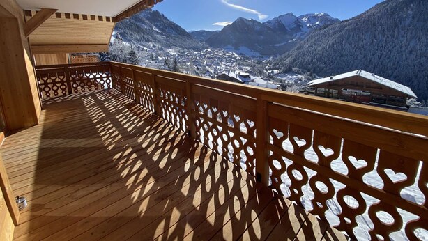 Un balcone in legno con vista su montagne innevate e un villaggio sottostante.