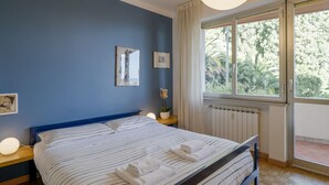 Una camera da letto con un letto, comodini, una finestra con tende e vista su del verde all'esterno.