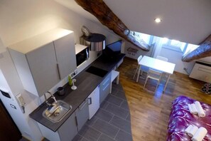Een compacte keuken met moderne apparaten, een zithoek met een tafel en stoelen, en een bed met een paarse deken.