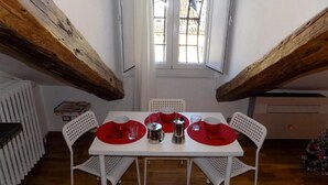 Una mesa de comedor con cuatro sillas, un ventanal con rejas y vigas de madera a la vista.