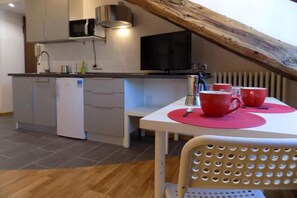 Een moderne keuken met witte kasten, een magnetron en een televisie. Er staat een eettafel met rode placemats en een stoel.