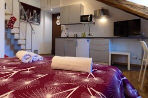 Een slaapkamer met een bed, een badkamer, een kitchenette en een trap.