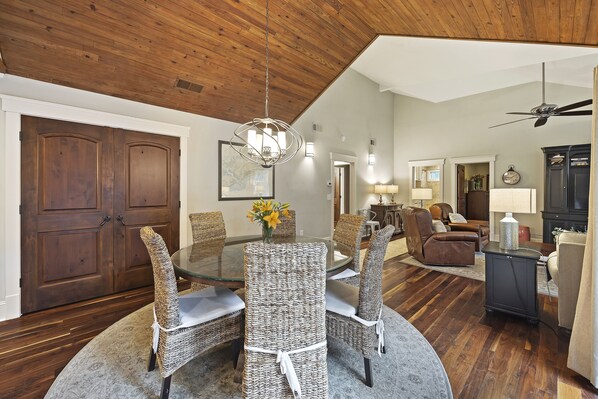 A dining area with a glass table and wicker chairs, a wooden ceiling, and a large wooden door. - Oceanwoods Kiawah West Beach 3BR Home, Seconds to Beach or Park! Great Location! (Kiawah Island)