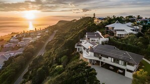 Un quartier résidentiel en bord de mer, avec des maisons modernes, une route et une vue sur l’océan au coucher du soleil.