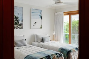 A bedroom with two beds, a ceiling fan, a window with curtains, and artwork on the walls. - Pool House And Wave Hill House Lennox head (Lennox Head)