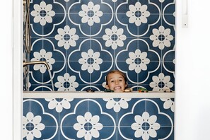 A bathroom with blue and white floral tiles, a shower area, and a child in a bathtub. - Pool House And Wave Hill House Lennox head (Lennox Head)