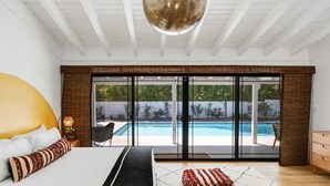 Ein Schlafzimmer mit einem großen Bett, Blick auf einen Swimmingpool und einer Glasschiebetür zu einem Außenbereich.