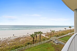 A beach view from a balcony with a railing, a sandy beach, ocean, and palm trees. - Summer Deals!! Gulf Front PCB within walking distance to attractions! (Panama City Beach)