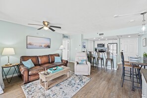 A living room with a brown leather sofa, a white armchair, a coffee table, and a dining area with a bar. - Summer Deals!! Gulf Front PCB within walking distance to attractions! (Panama City Beach)