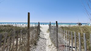 Un sentier de sable qui longe la plage et mène à l’océan, bordé de clôtures en bois et de parasols de plage.