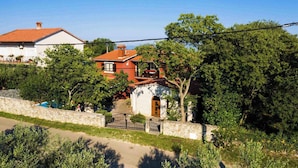 Une villa avec un toit recouvert de tuiles rouges, un mur en pierre et une végétation luxuriante.