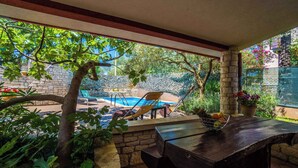 Un espace extérieur abrité comprenant une piscine, des chaises longues et une table sur laquelle est disposé un panier de fruits.