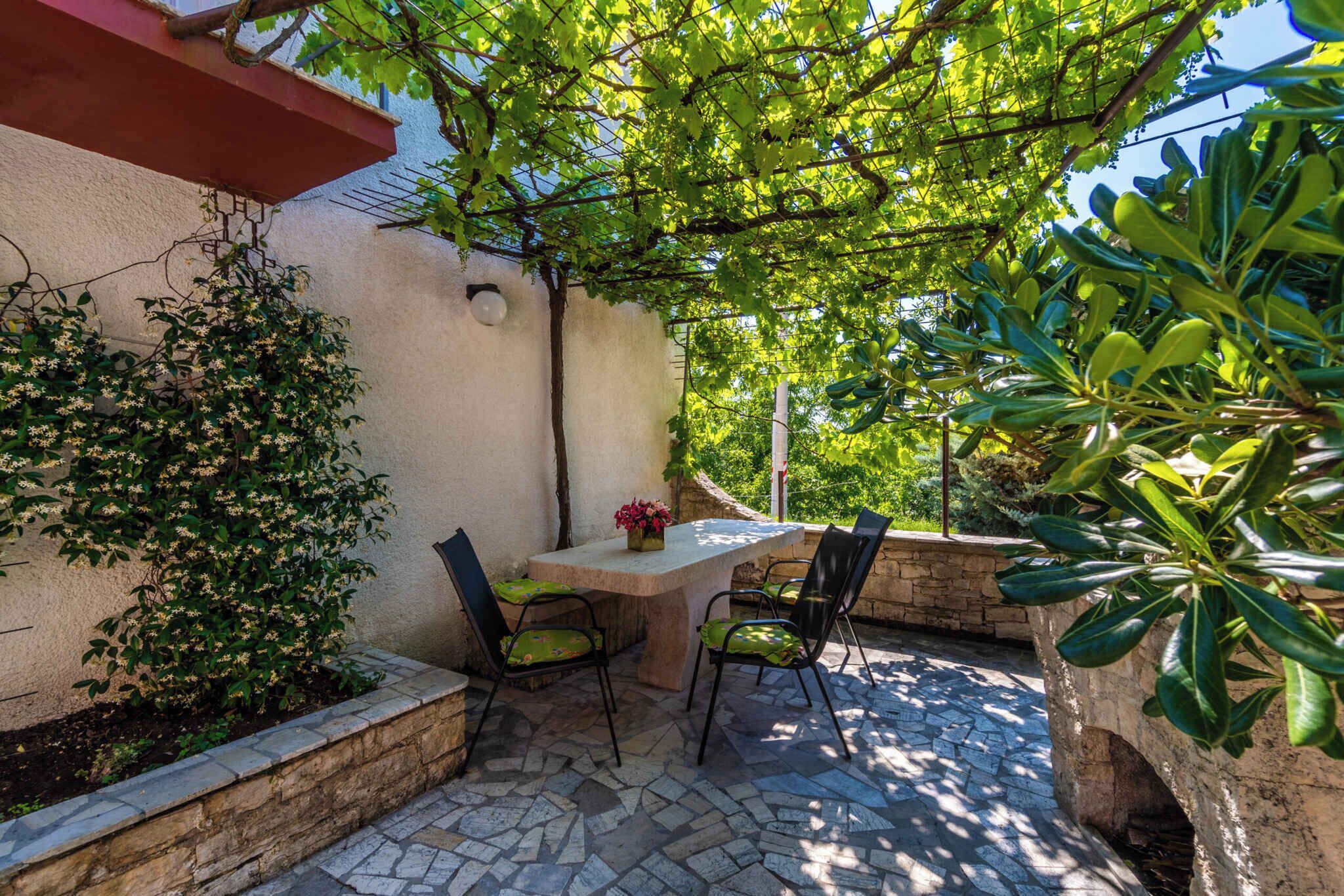 An outdoor patio with a stone table and chairs, surrounded by greenery and a stone wall.