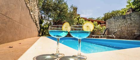 Två glas blå cocktail med citronskivor på ett bord vid poolkanten.