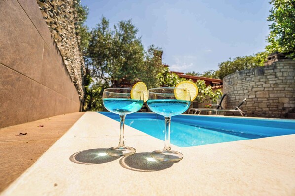 Two glasses of blue cocktail with lemon slices on a poolside table.