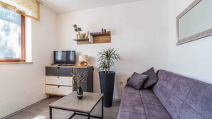 A modern living room with a sofa, a coffee table, a TV on a stand, a potted plant, and a shelf with decorative items. - Holiday apartment with pool and air conditioning (Krnica)