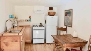 A compact kitchen with wooden cabinets, a white refrigerator, a stove, and a dining table with chairs. - Sunnybrae Garden Studio (Arcata)