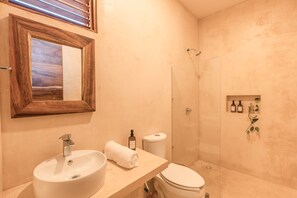 A bathroom with a wooden-framed mirror, a sink, a toilet, and a shower area. - Xcalak paradise Hotel (Xcalak)