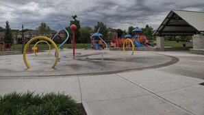 A playground with various play structures, a covered seating area, and a cloudy sky.
