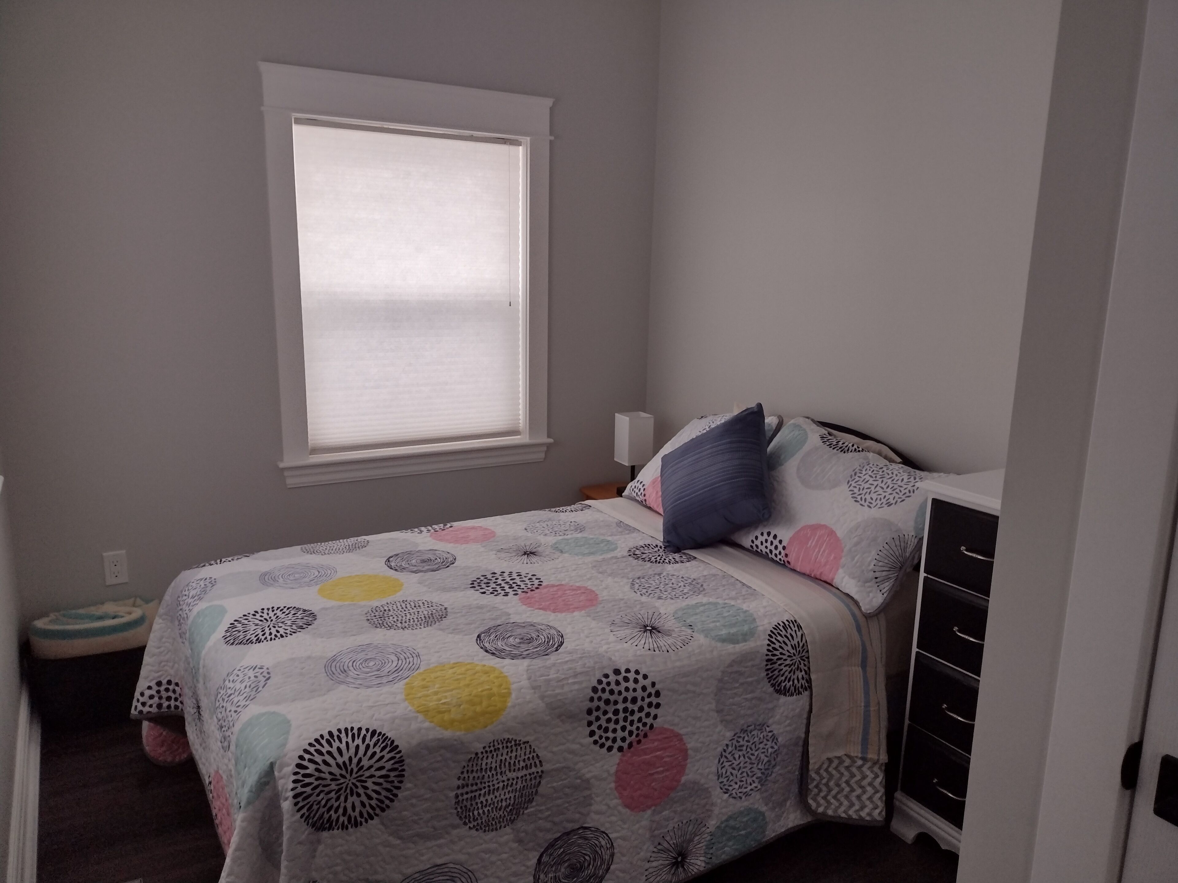 A bedroom with a bed, a window, a dresser, and a small bedside table.